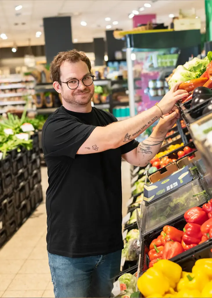 Mitarbeiter im Bioladen in Ulm räumt frisches Obst und Gemüse ein, Arbeiten im nachhaltigen Einzelhandel